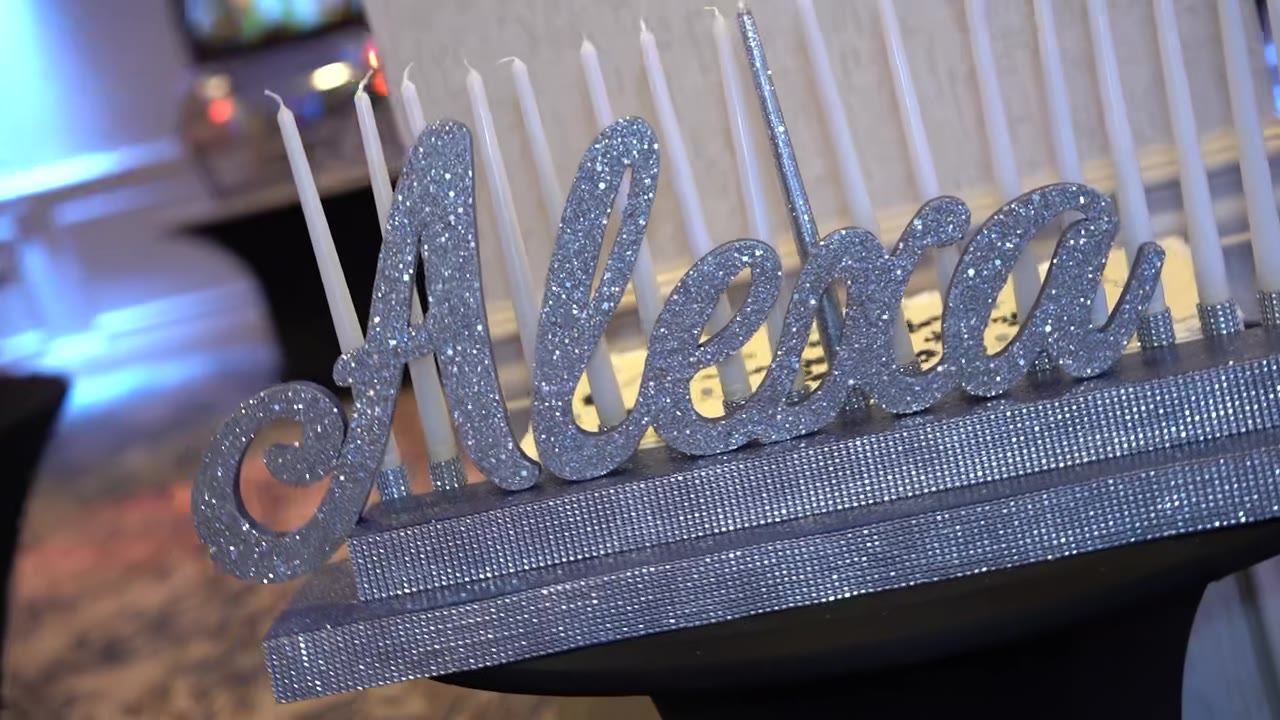 A sixteen-candle board in silver glitter with Alexa&rsquo;s name across the front, candles still unlit before the ceremony.