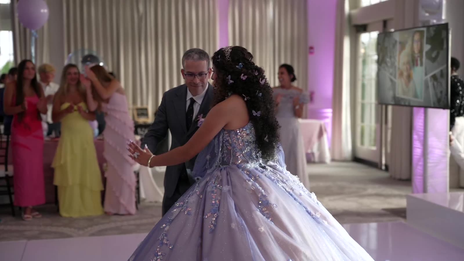 A quincea&ntilde;era entrance: Bella in a lilac ballgown led onto the floor by her father while the room watches.