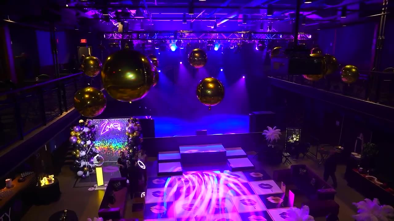 The room before doors: gold mirror balls over a lit LED dance floor, purple uplighting and a neon backdrop.